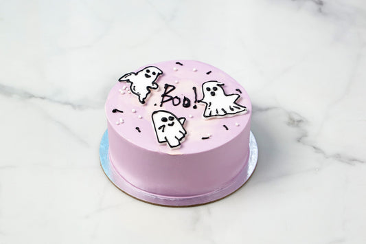 Pink cake with ghost and 'Boo' decorations on a marble surface