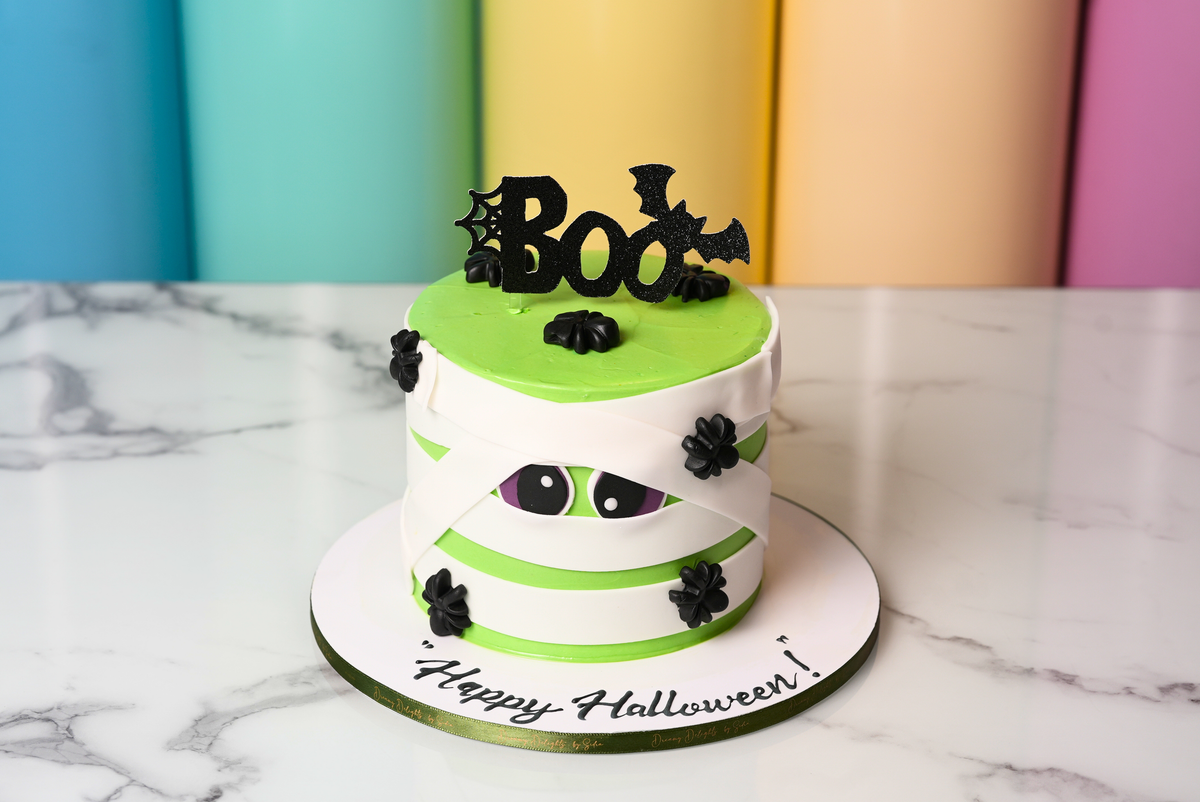 Green Halloween Boo cake with white mummy wraps, cartoon eyes, and black spiders by Dreamy Delights by Sidra in Dubai.