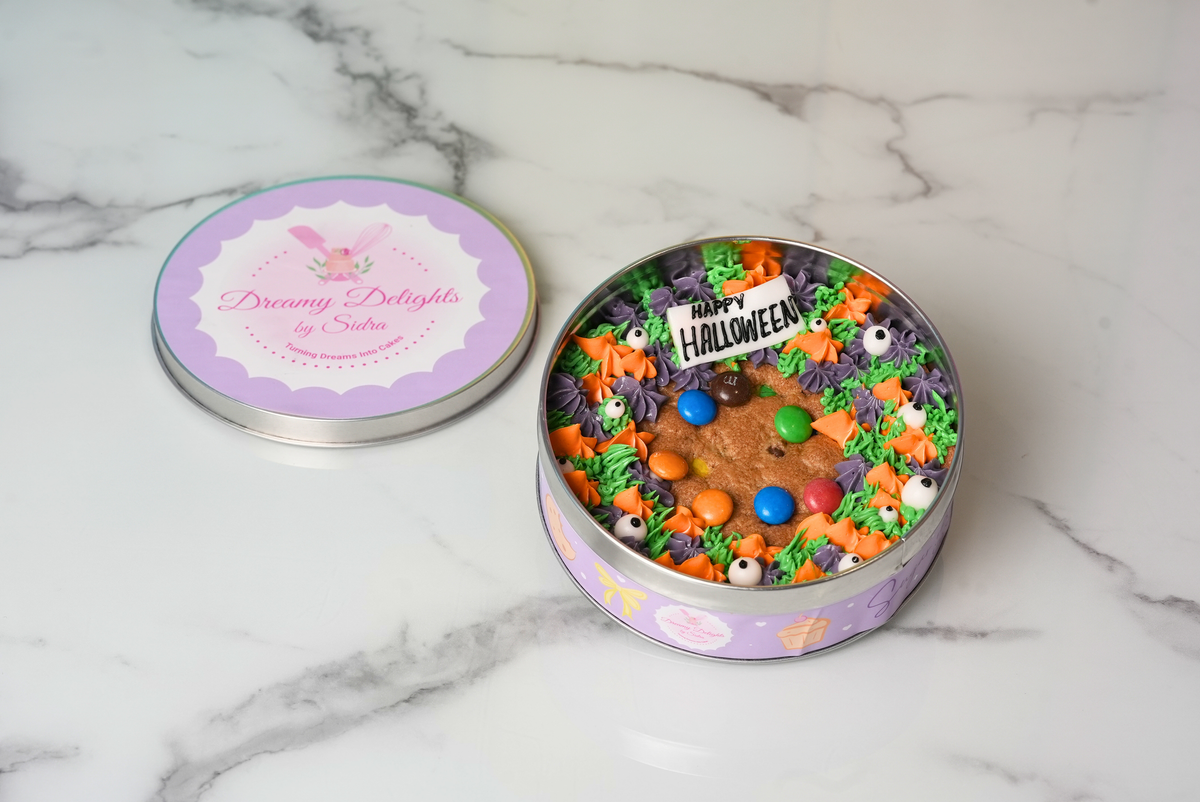 Halloween chocolate chip cookie topped with colourful frosting, candy pieces, and spooky eyes in a decorative tin by Dreamy Delights by Sidra in Dubai.