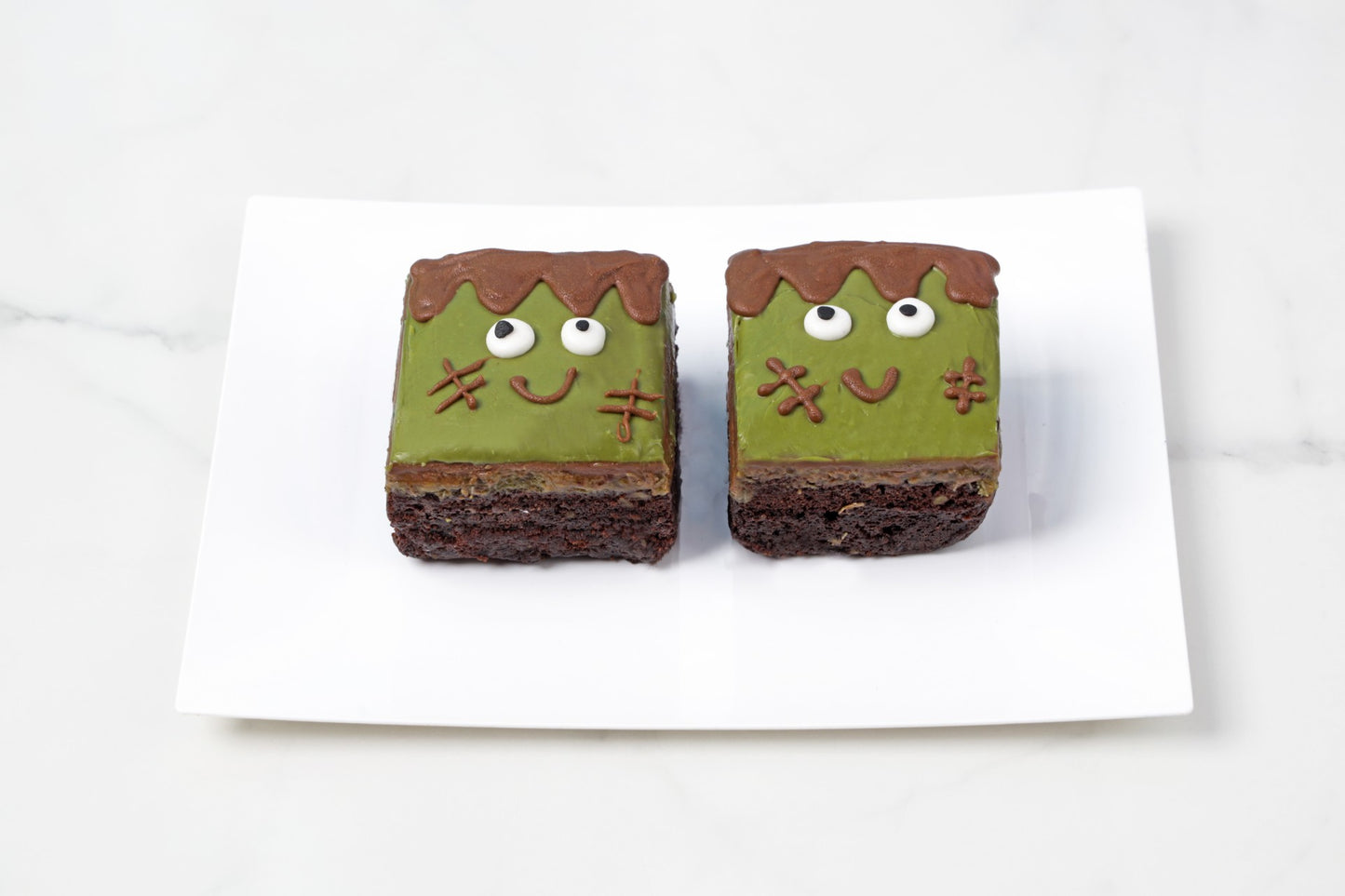 Two brownies with green icing and face decorations on a white background
