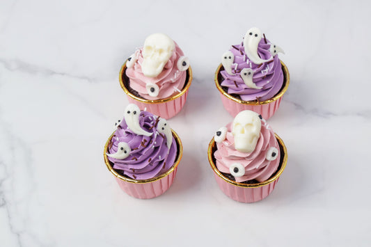 Four cupcakes with purple and pink frosting and ghost decorations on a white background