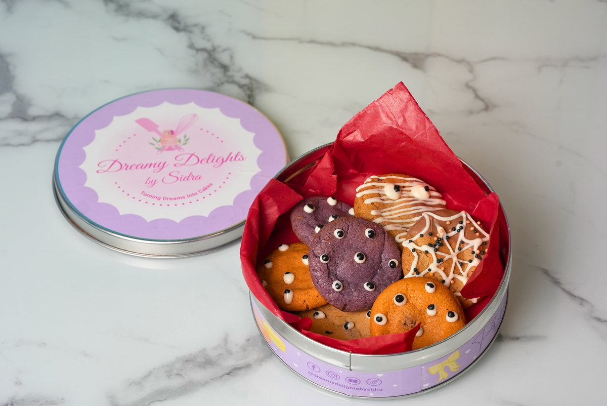 Halloween Spooky Eyes Cookie Tin filled with purple and golden cookies decorated with edible eyes and chocolate spiderweb designs by Dreamy Delights by Sidra in Dubai.