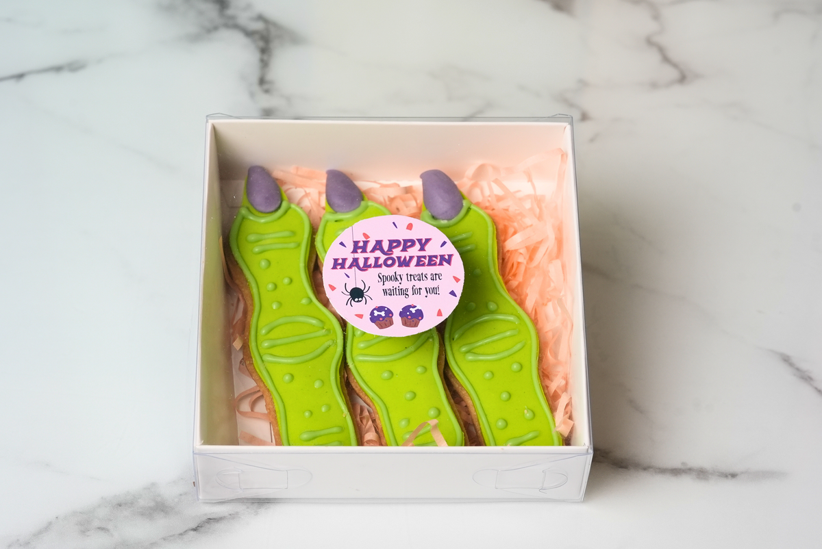 Three green Halloween witch finger cookies with purple tips in a gift box by Dreamy Delights by Sidra in Dubai.