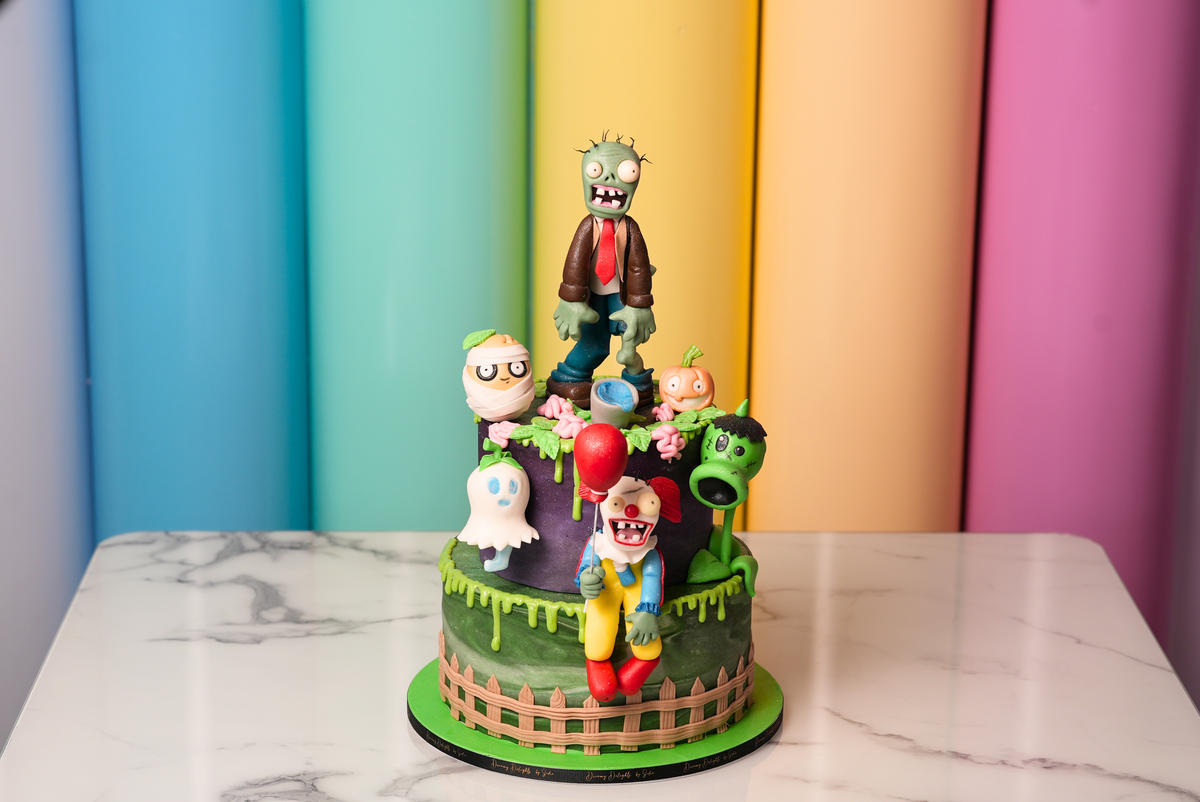 Two-tier Halloween zombie cake with spooky character toppers, ghosts, pumpkins, and green drips by Dreamy Delights by Sidra in Dubai.