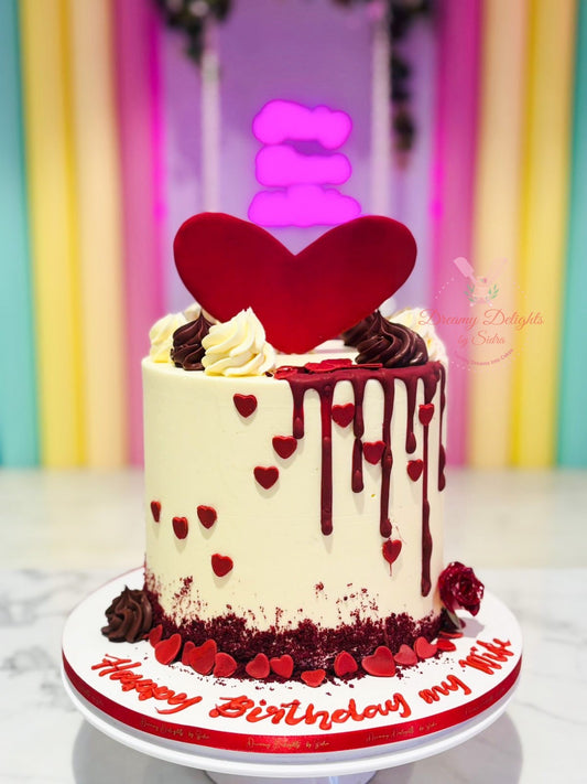 Decorative birthday cake with red heart topper and 'Happy Birthday' message against a colorful curtain background.