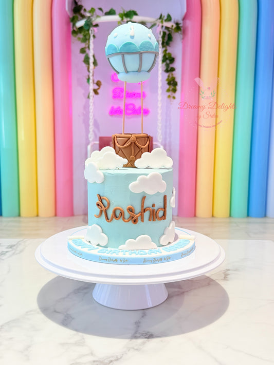 Hot air balloon birthday cake with blue frosting, fondant clouds and balloon topper by Dreamy Delights by Sidra in Dubai.