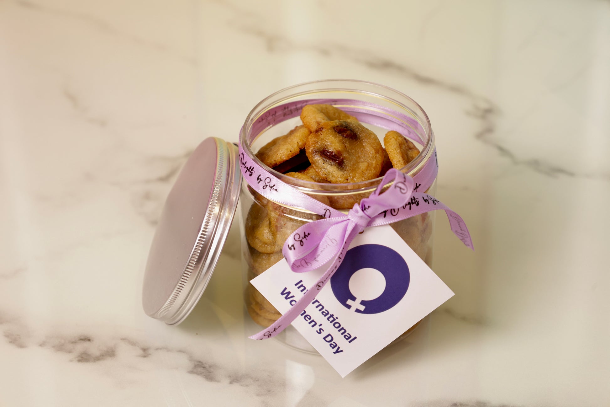 Jar of cookies with a purple ribbon and tag on a marble surface