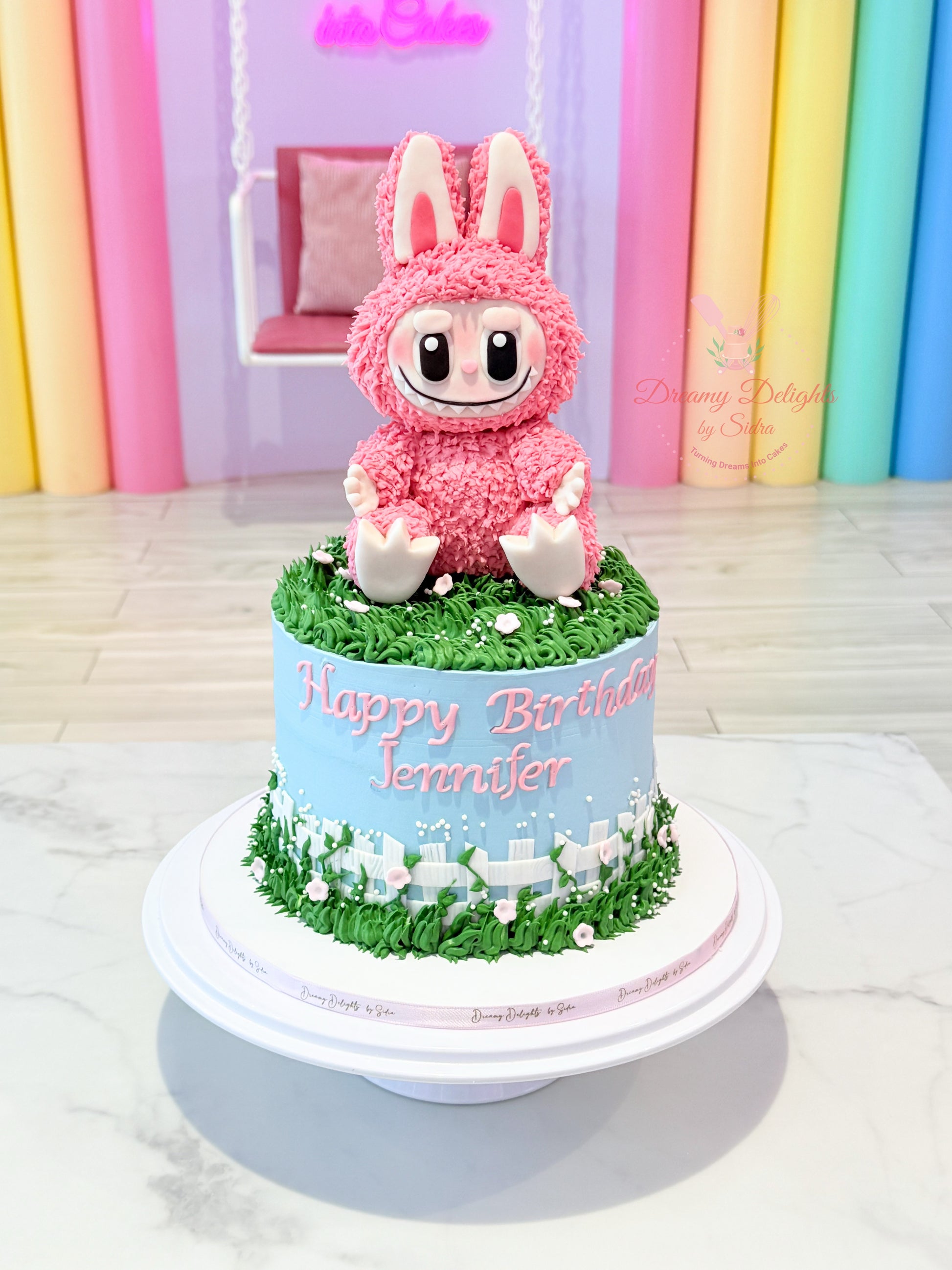 Birthday cake with a pink character on top against a colorful curtain background