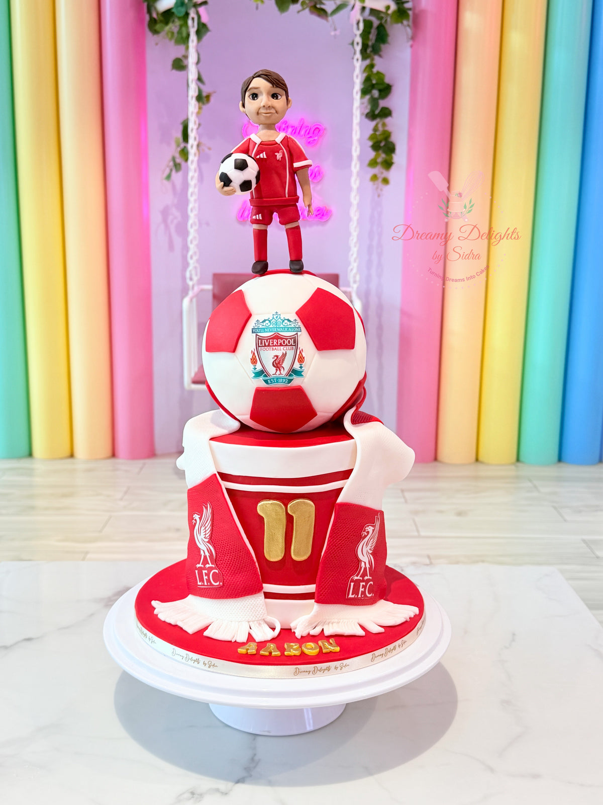 Liverpool Football Club Cake with red and white football topper, footballer figurine and scarf decorations in Dubai