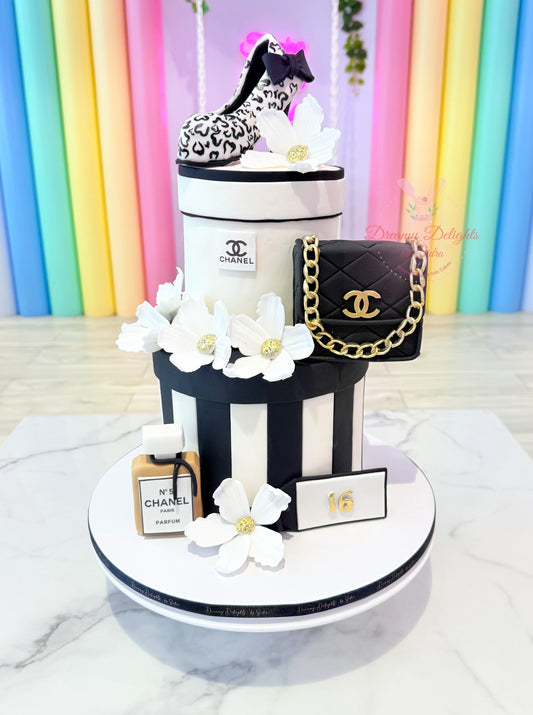 Chanel-themed cake with black handbag, flowers, and bottle against a colorful background