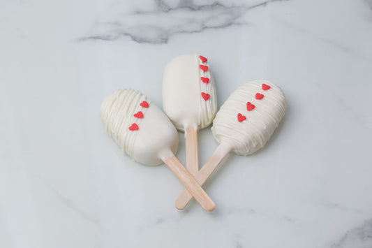 Mini heart-shaped Valentine’s Day cakesicles with white coating and red heart details by Dreamy Delight by Sidra