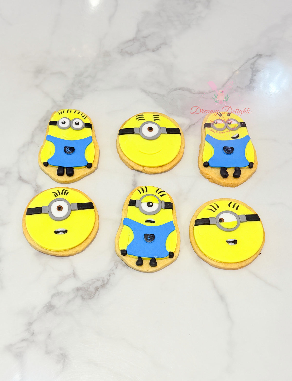 Minion theme cookies decorated with yellow characters, blue outfits and playful expressions by Dreamy Delights by Sidra in Dubai.