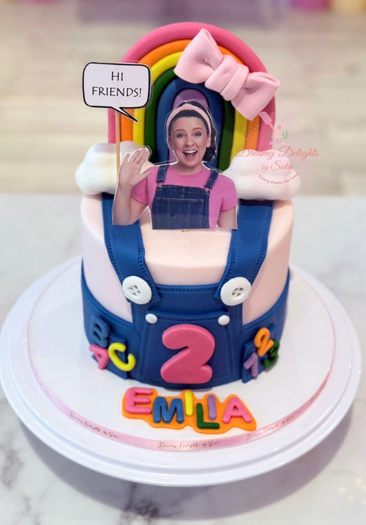 Ms. Rachel cake Dubai with colourful rainbow, pink bow and blue overall design by Dreamy Delights by Sidra