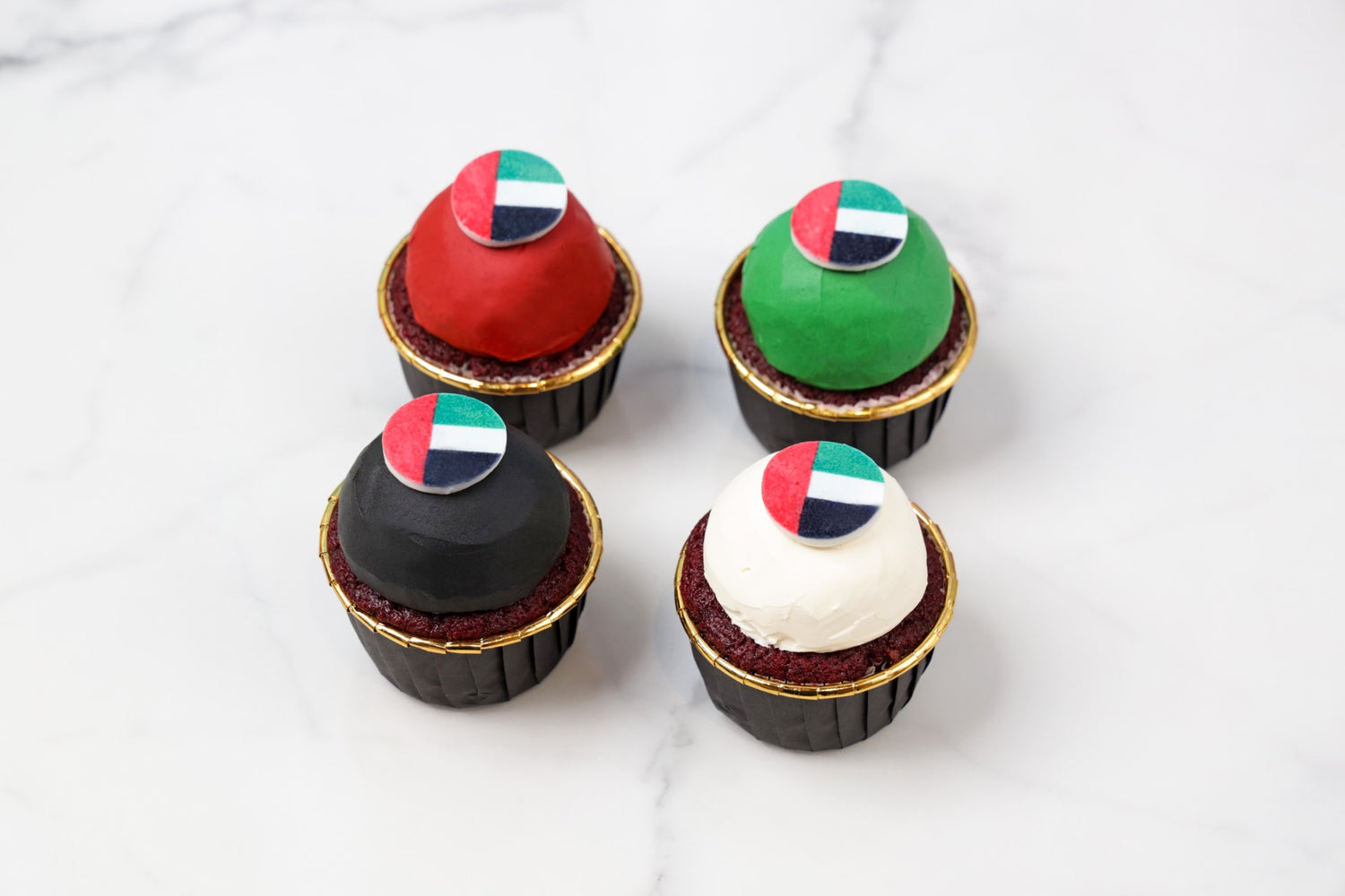 four cupcakes with colorful flags on a white marble surface