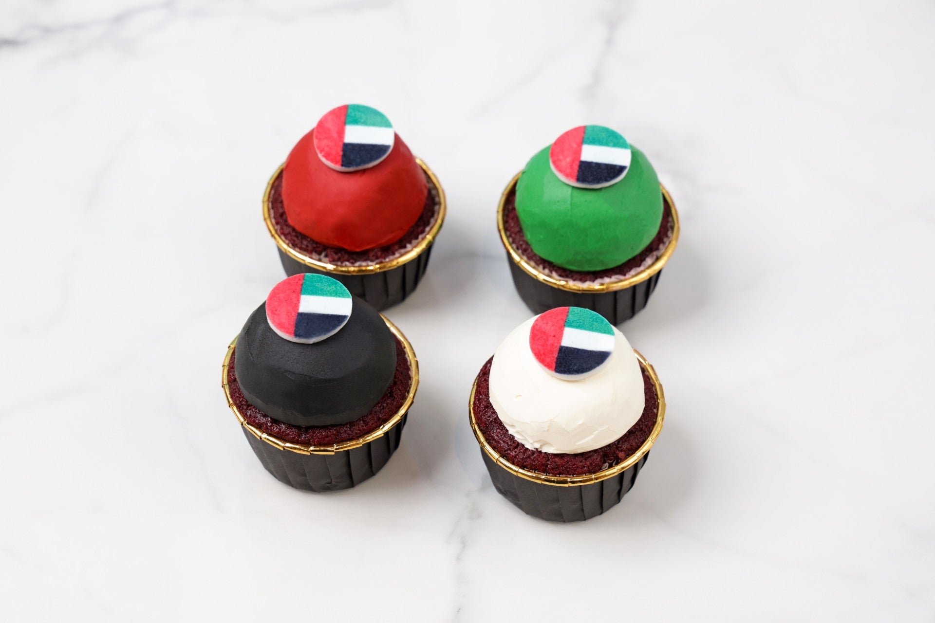 four cupcakes with colorful flags on a white marble surface