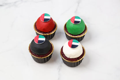 four cupcakes with colorful flags on a white marble surface