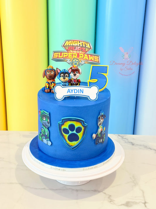Blue birthday cake with Paw Patrol figures and decorations against a colorful curtain background