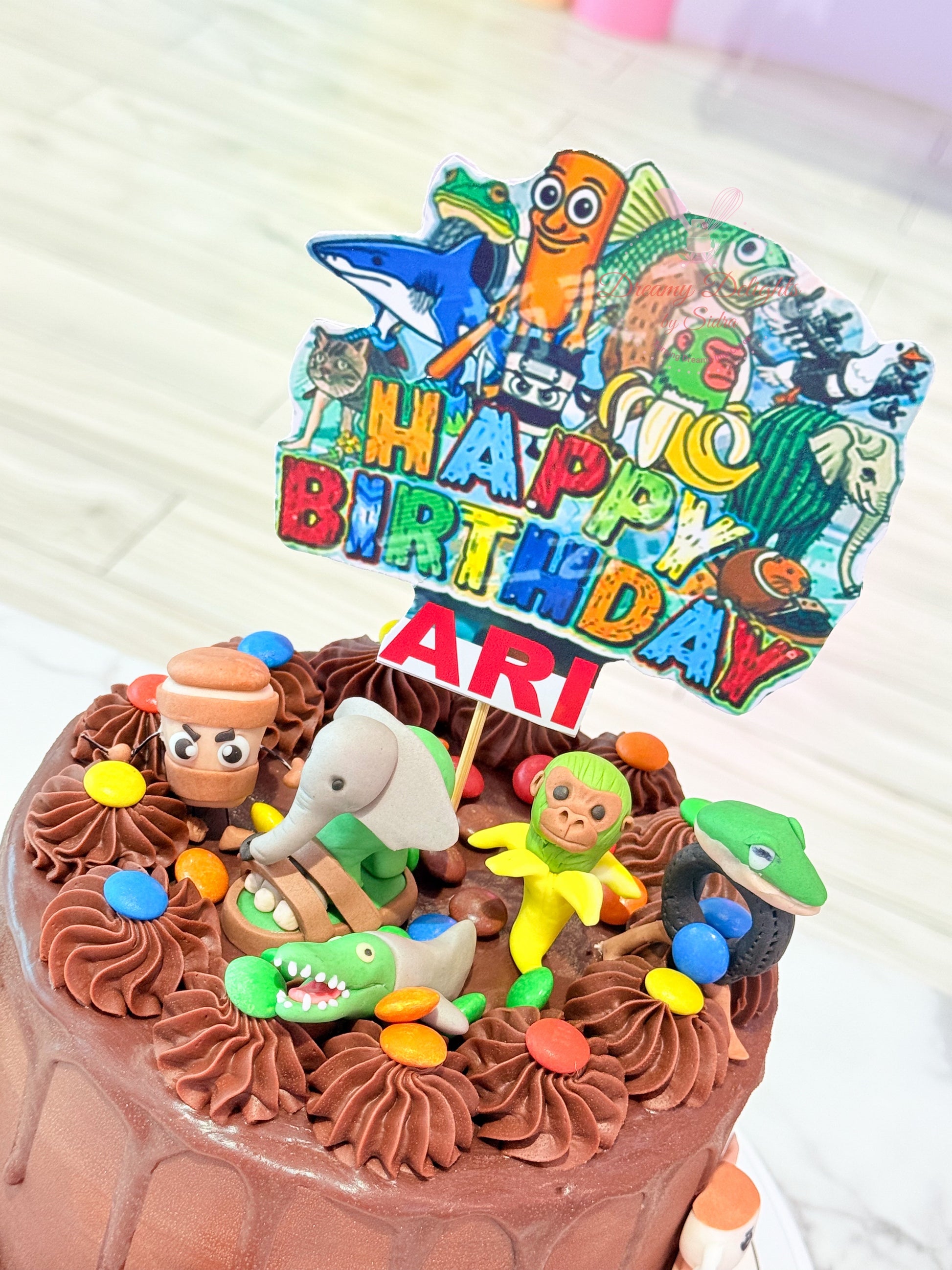 Birthday cake with colorful figurines and 'Happy Birthday Art' topper.