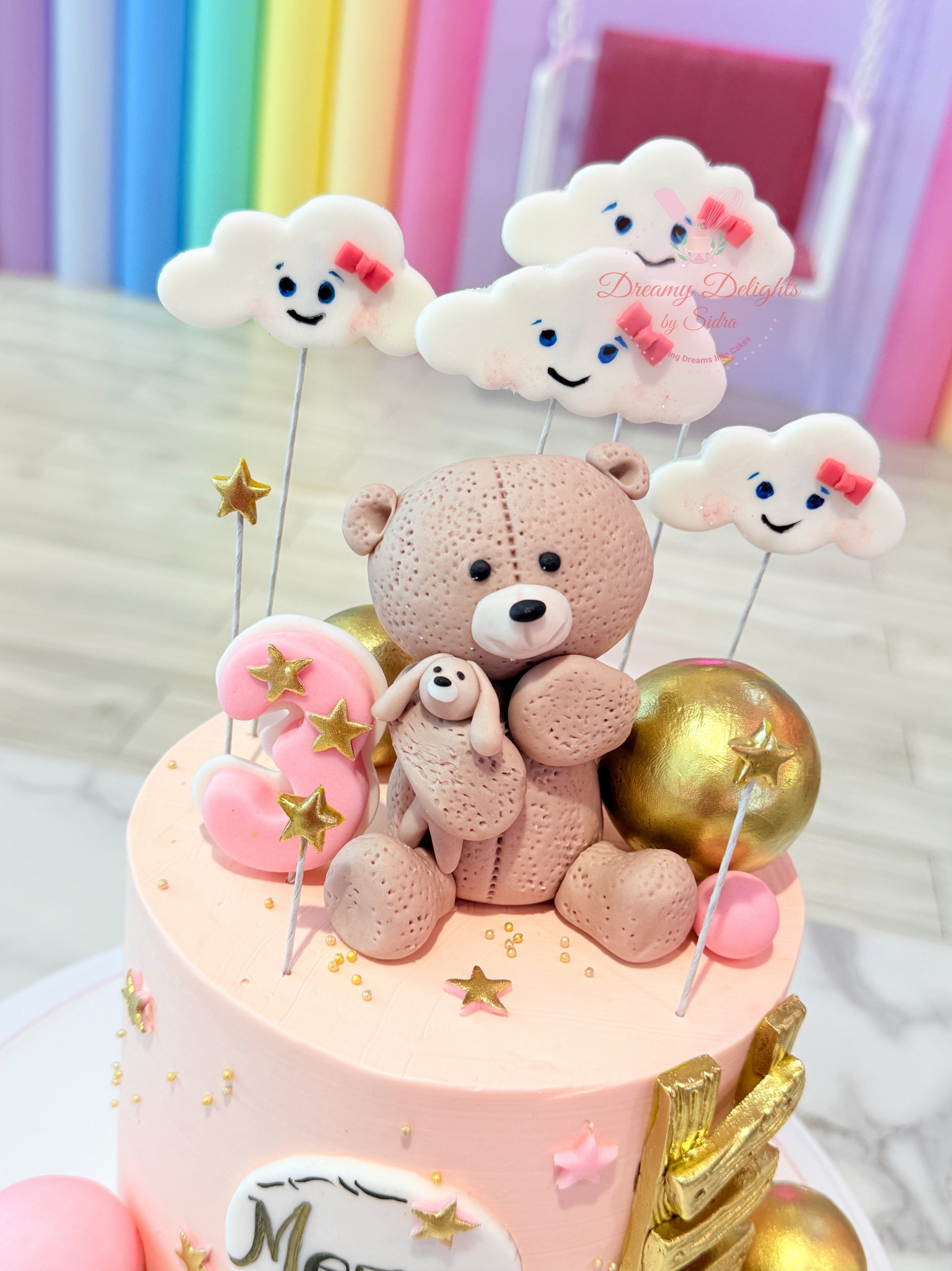 Decorative cake with teddy bear and cloud toppers against a colorful background