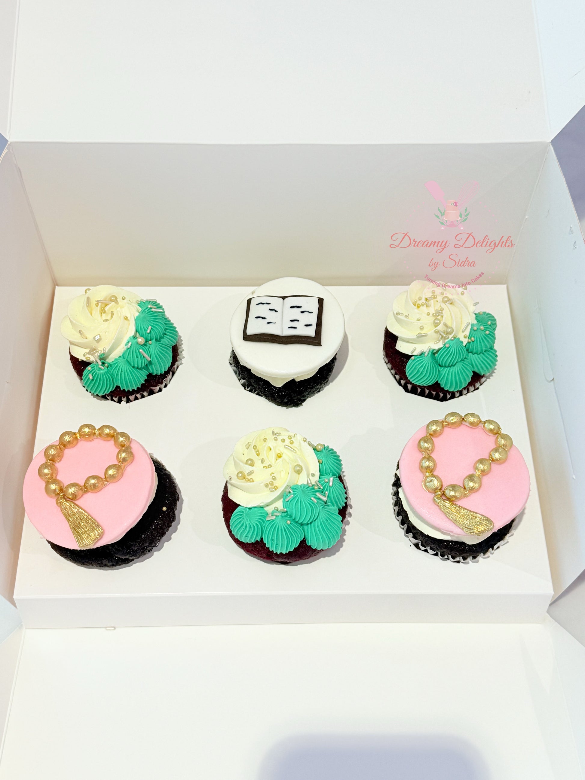Box of six decorated cupcakes with various designs on a white background