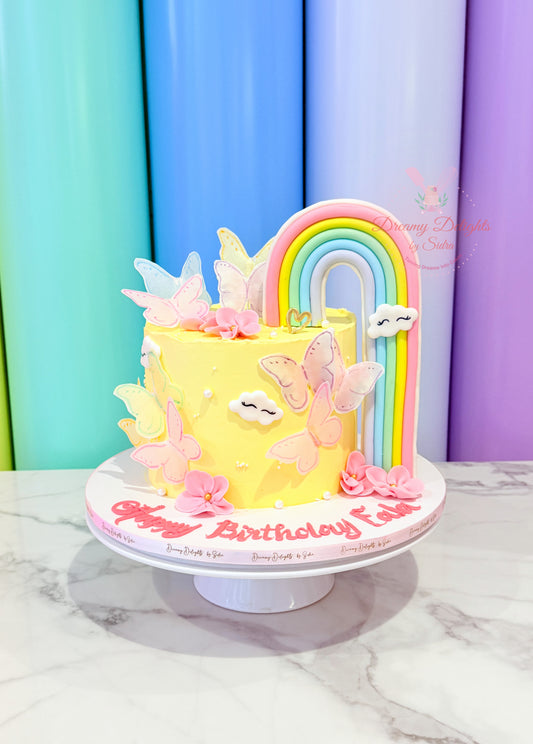 Colorful birthday cake with rainbow and butterflies on a marble surface.
