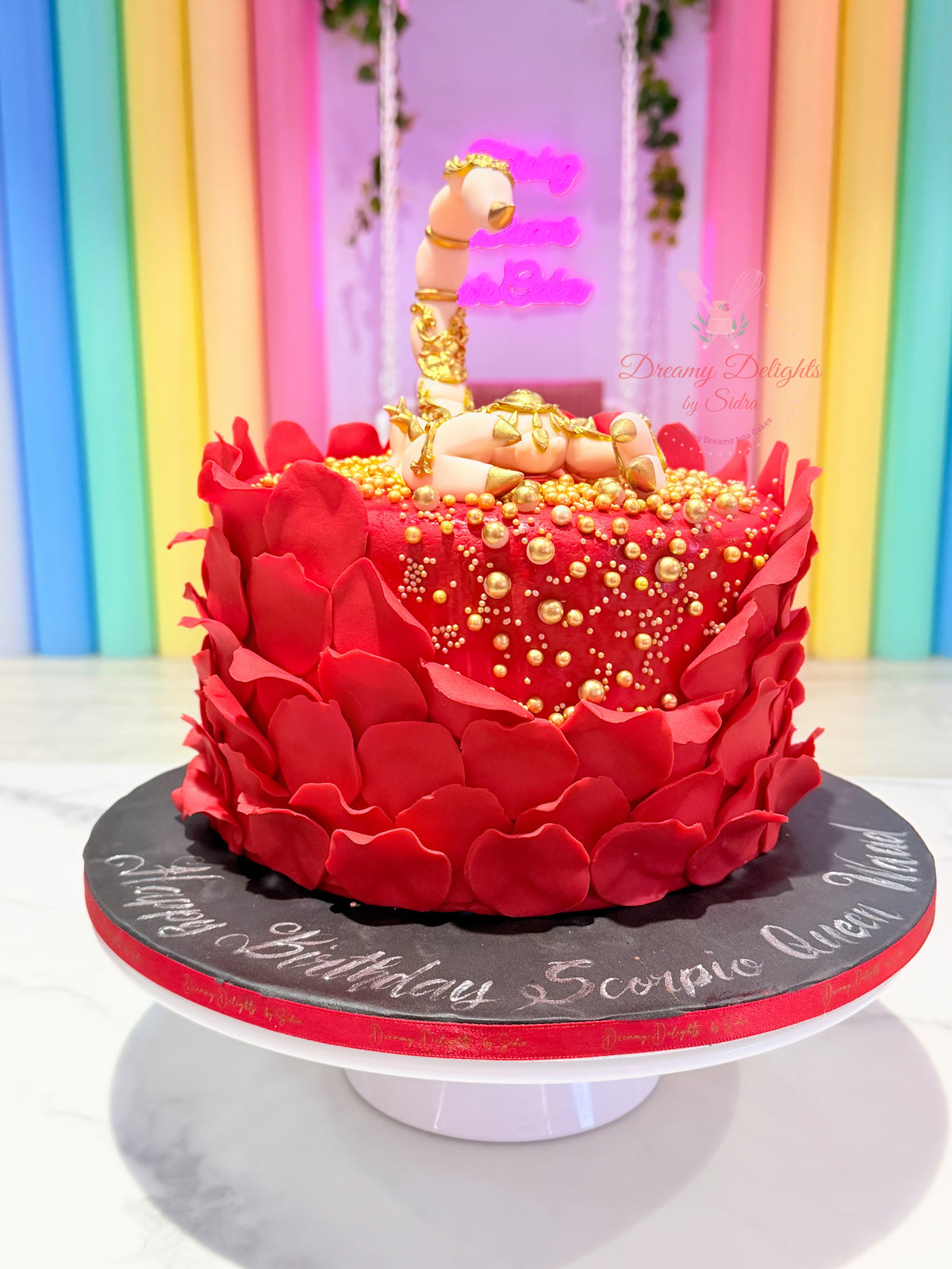 Scorpio Queen Cake with red petals, gold details and Scorpio topper for a birthday celebration