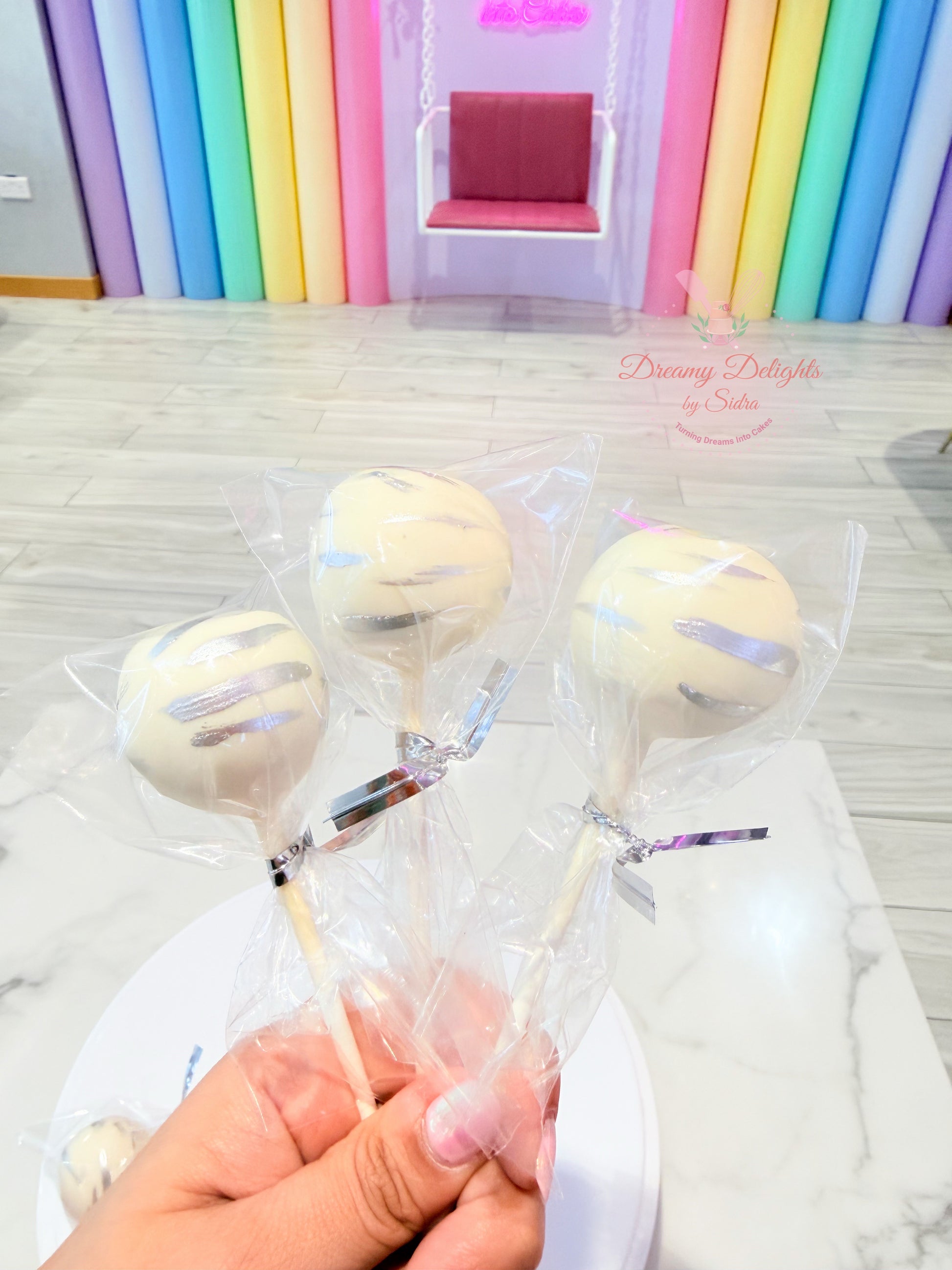 Elegant white chocolate cake pops with edible silver brush strokes individually wrapped for celebrations in Dubai.