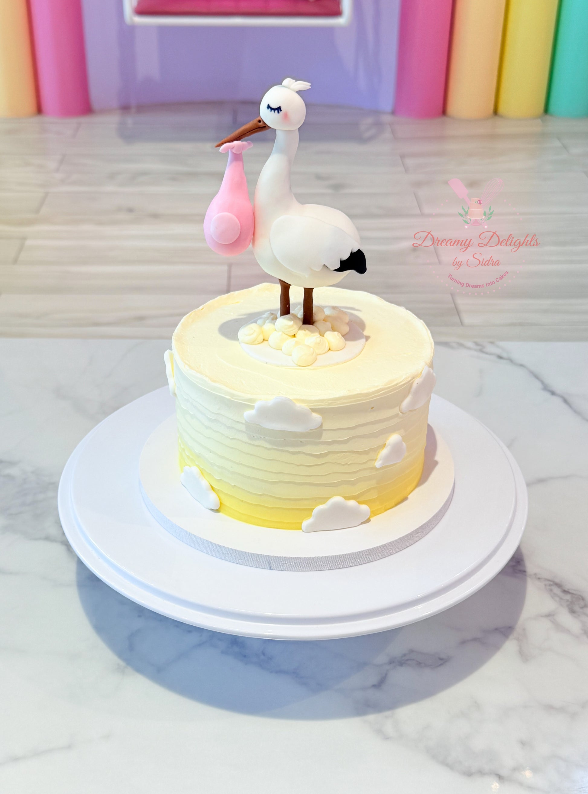 Decorative cake with a stork and baby in a pink bag on a marble surface.