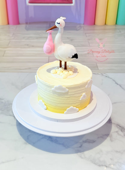 Decorative cake with a stork and baby in a pink bag on a marble surface.
