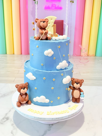 Three-tiered blue cake with teddy bear decorations against a colorful curtain background