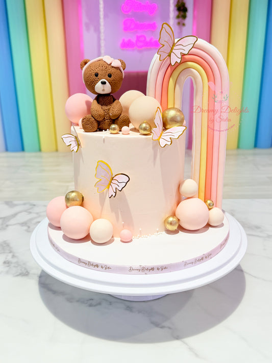 Children's birthday cake with teddy bear, rainbow, and colorful decorations on a marble surface.