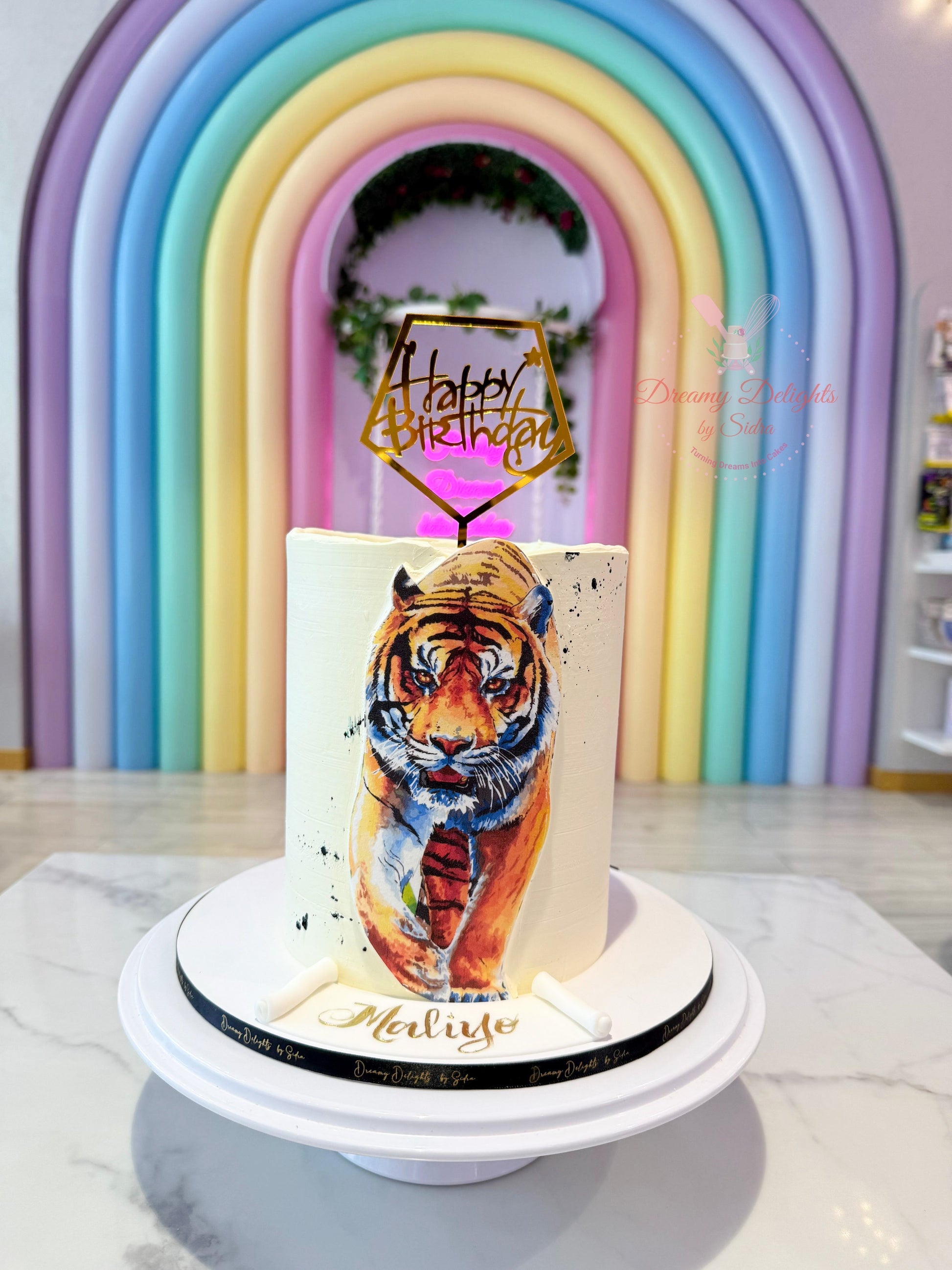 Cake with tiger design and 'Happy Birthday' topper against a colorful arch background