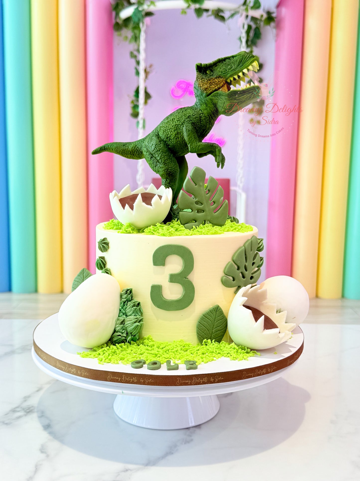 Trex dinosaur cake for boys with jungle theme design, green dinosaur topper, cracked egg decorations, and kids birthday celebration setup