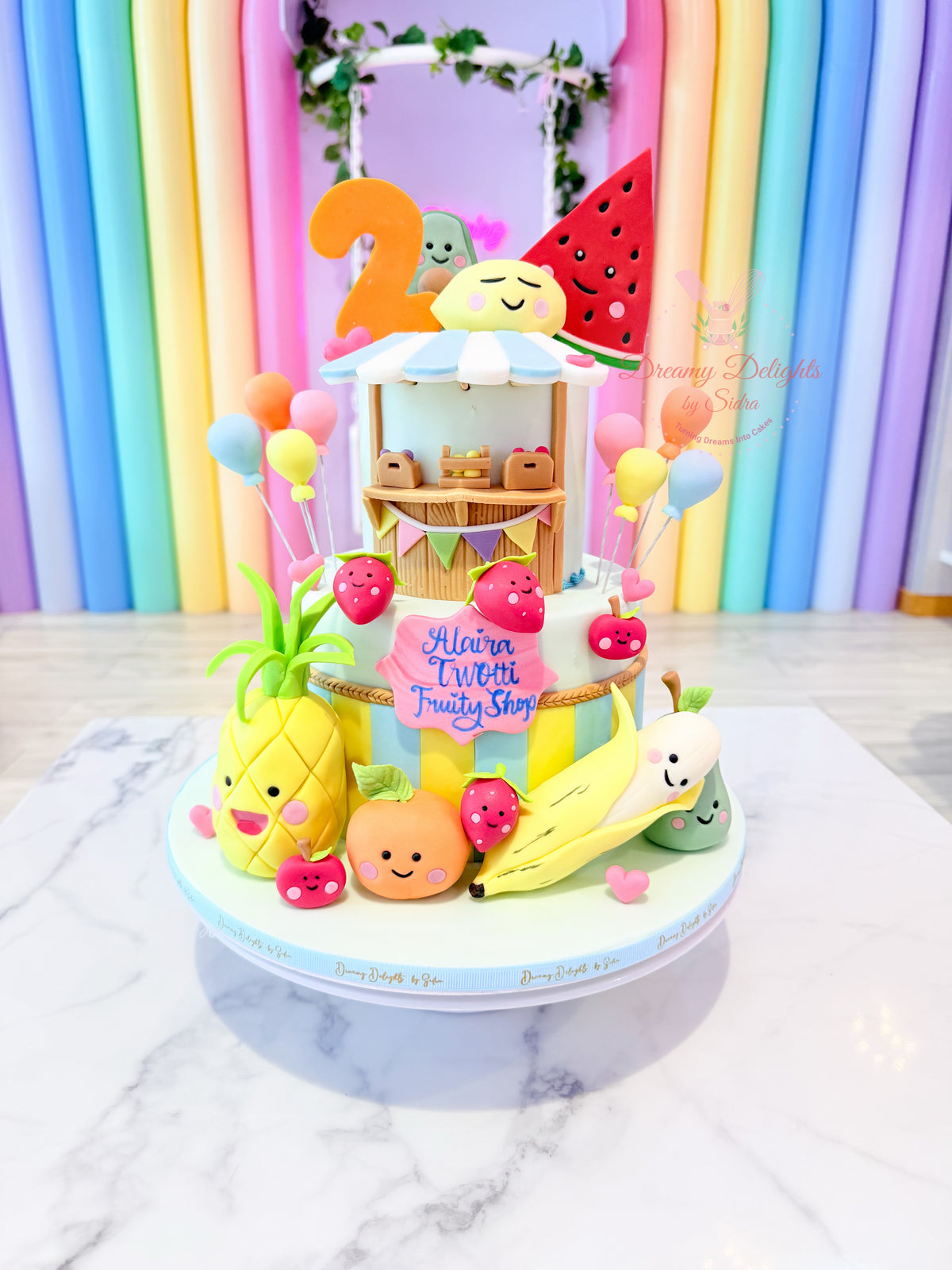 Two-ty Fruity fruit shop birthday cake Dubai with cute smiling fruits, pastel balloons and colourful decorations by Dreamy Delights by Sidra