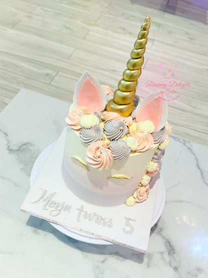 Unicorn-themed birthday cake with gold horn and pink ears on a marble surface.