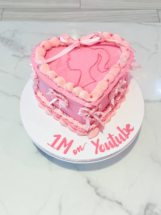 Heart-shaped pink cake with a silhouette of a girl and '1M on Youtube' text on a marble surface.
