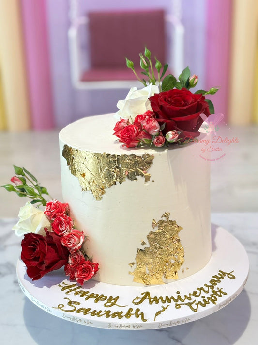 Decorative cake with flowers and gold leaf design on a white surface.